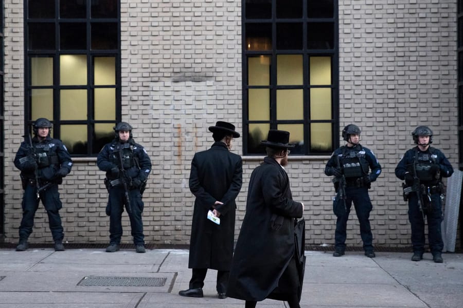 Orthodox Jewish men pass New York City police guarding a Brooklyn synagogue before a funeral for Mosche Deutsch, a rabbinical student from Brooklyn who was killed in a shooting at a Jersey City, N.J. market, Dec. 11, 2019